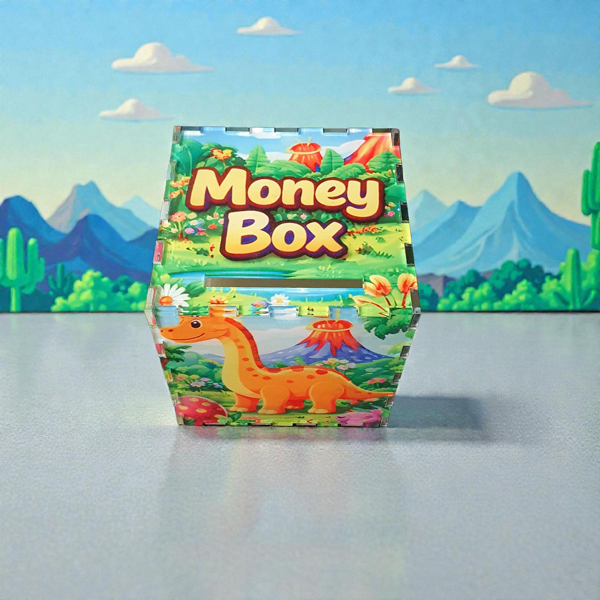Angled front view of dinosaur money box with “Money Box” text on lid and orange dinosaur illustration on front. Bright, playful children’s savings box set against illustrated mountain background.