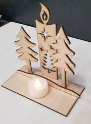 Wooden candle holder with tree designs and a lit candle on a white surface.