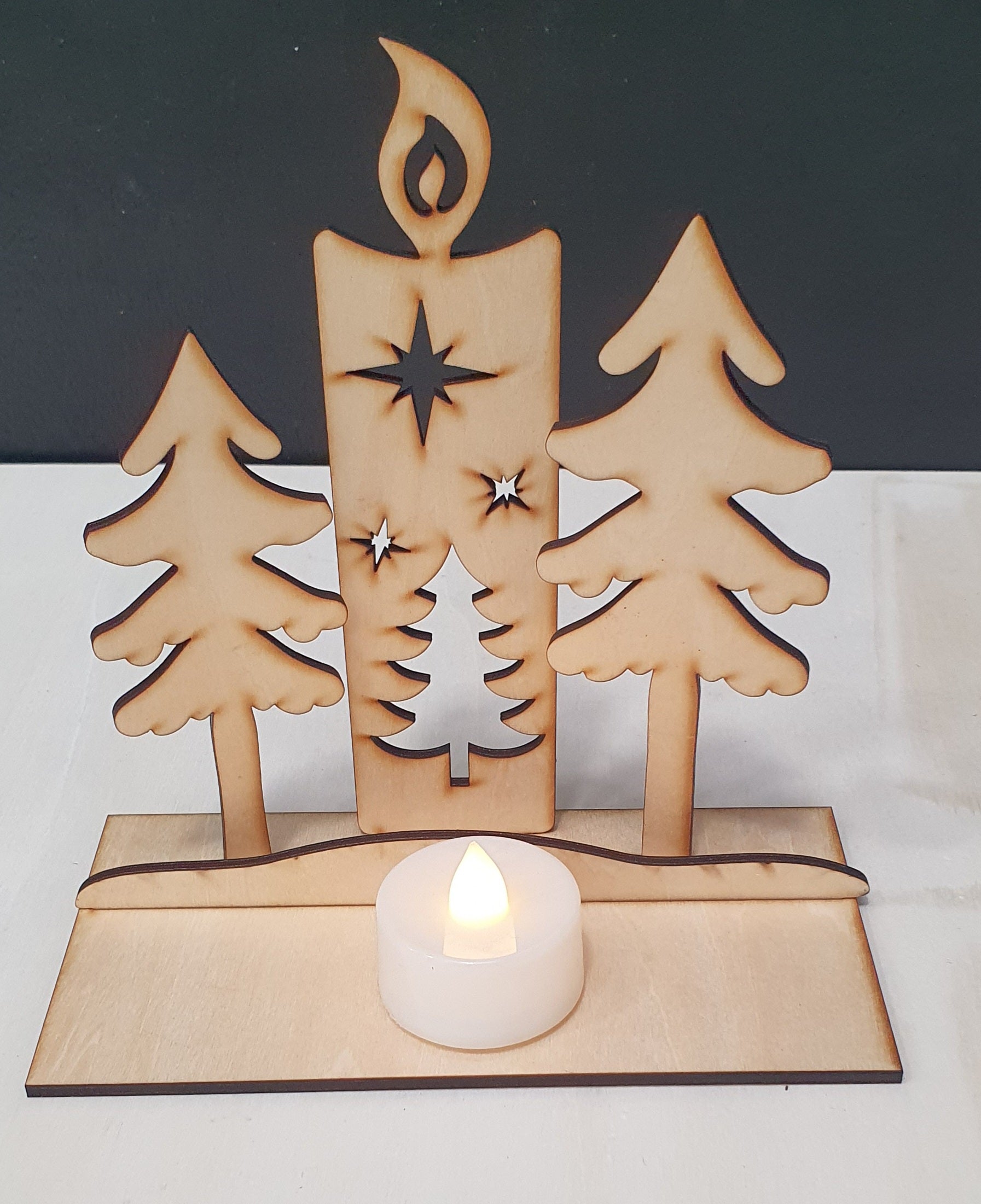 Wooden candle holder with trees and a star, featuring a lit tealight on a white background.