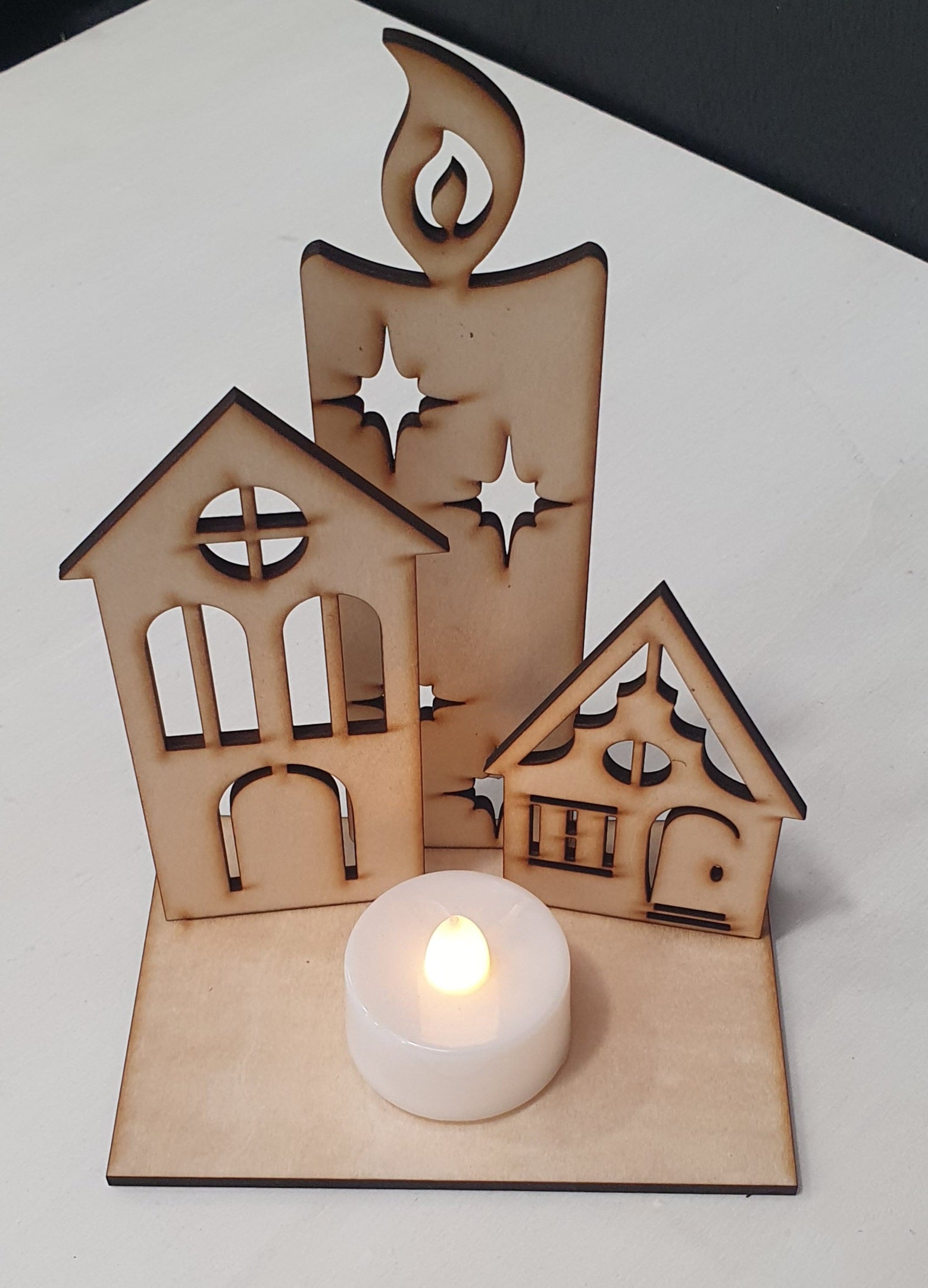 Decorative wooden house-shaped candle holder with a small candle inside on a white background