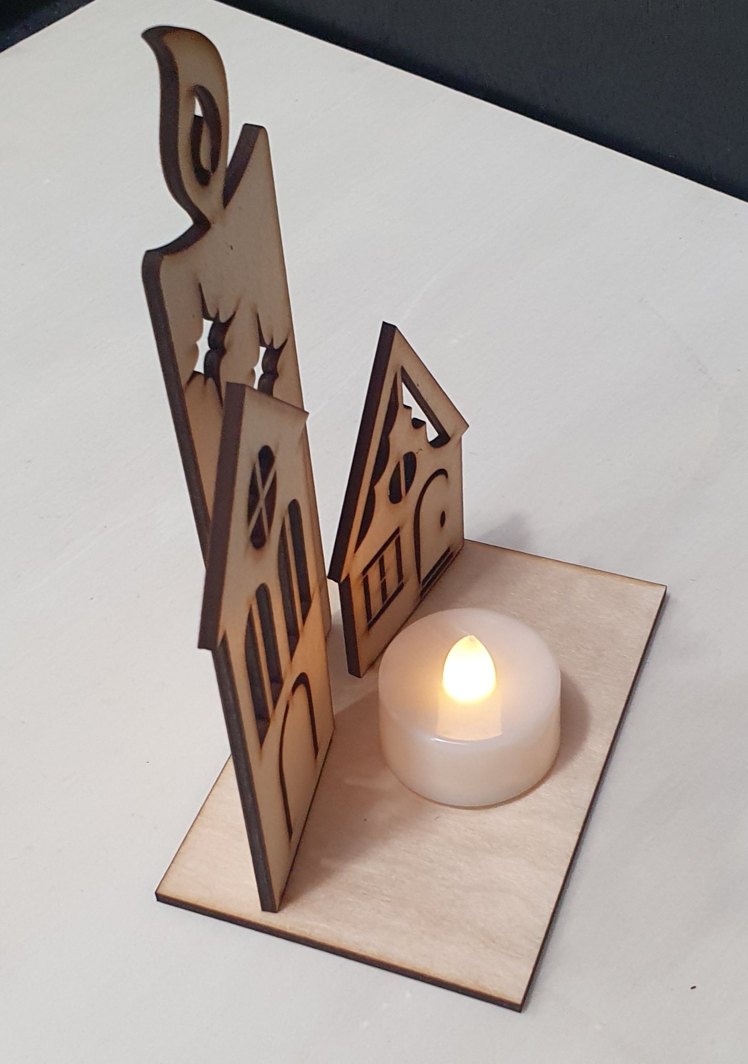 Wooden house-shaped candle holder with a lit candle on a white surface