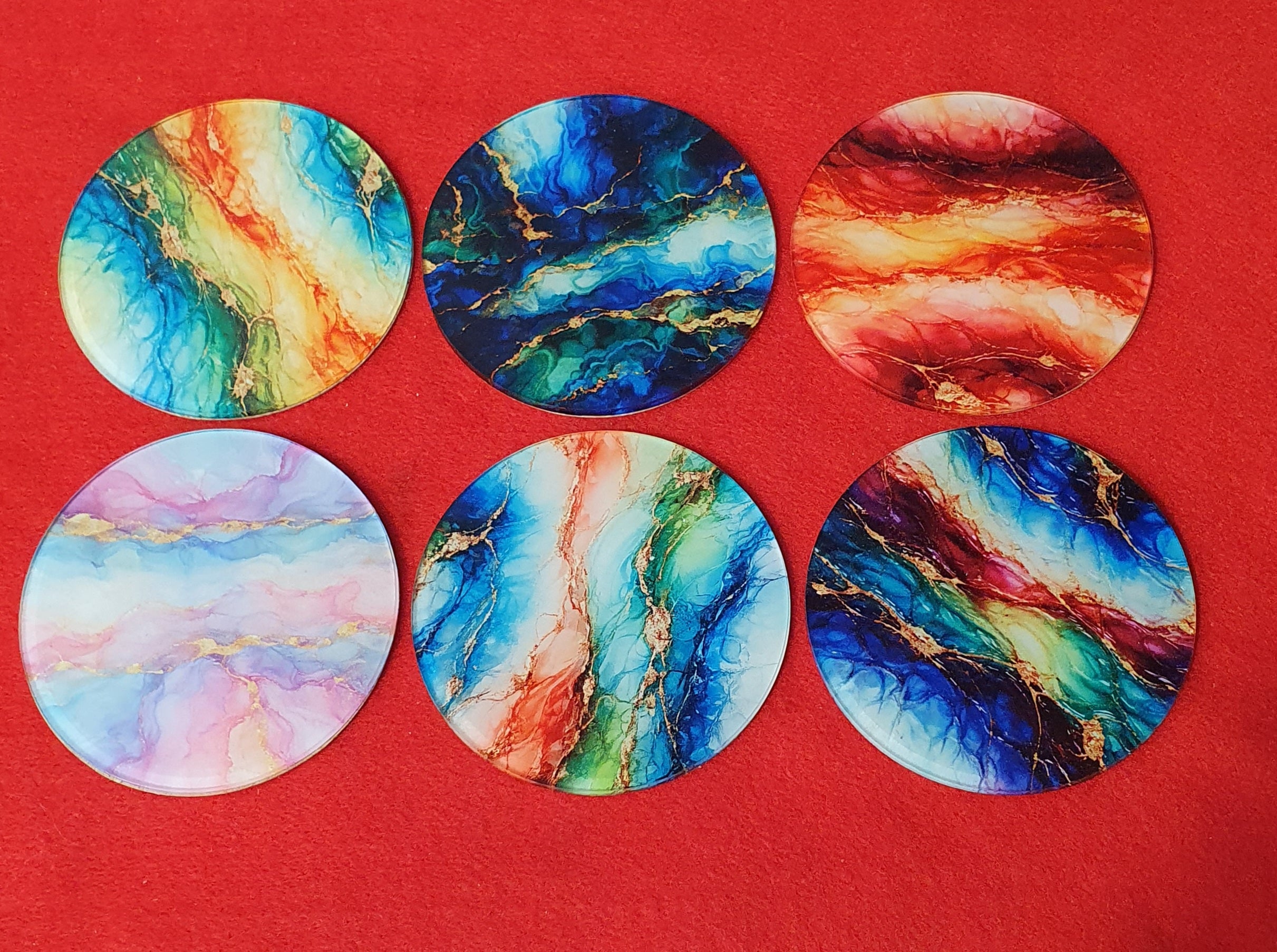 Abstract marble print round drink coasters set with colorful alcohol ink designs in blue, teal, red and gold on cork backing