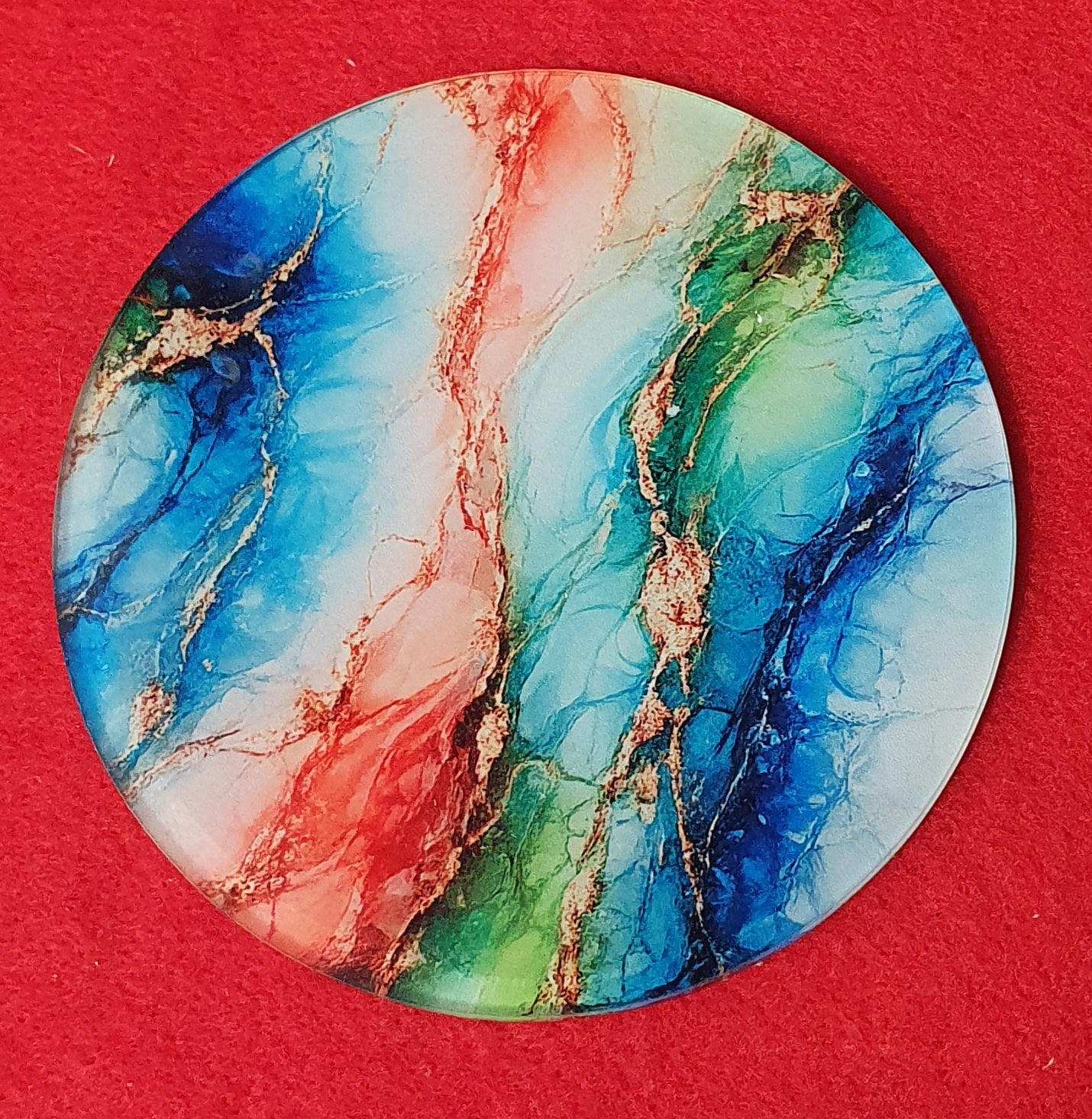 Round abstract alcohol ink coaster featuring blue, teal, red and gold marble effect with cork backing