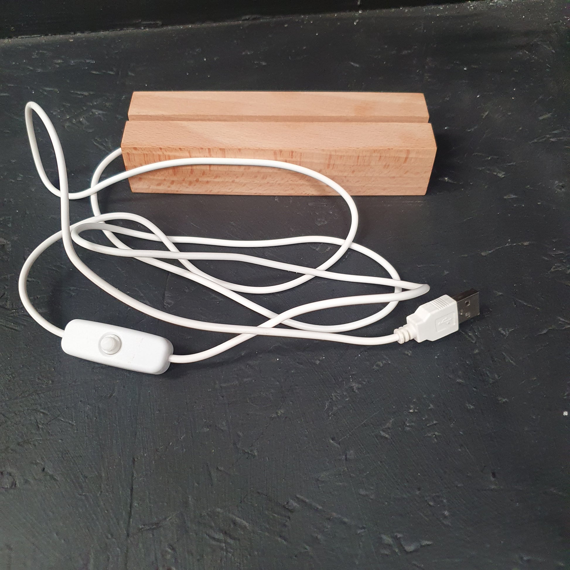 A white USB charging cable with an inline switch and wooden end caps, shown on a dark textured surface next to two small wooden blocks.