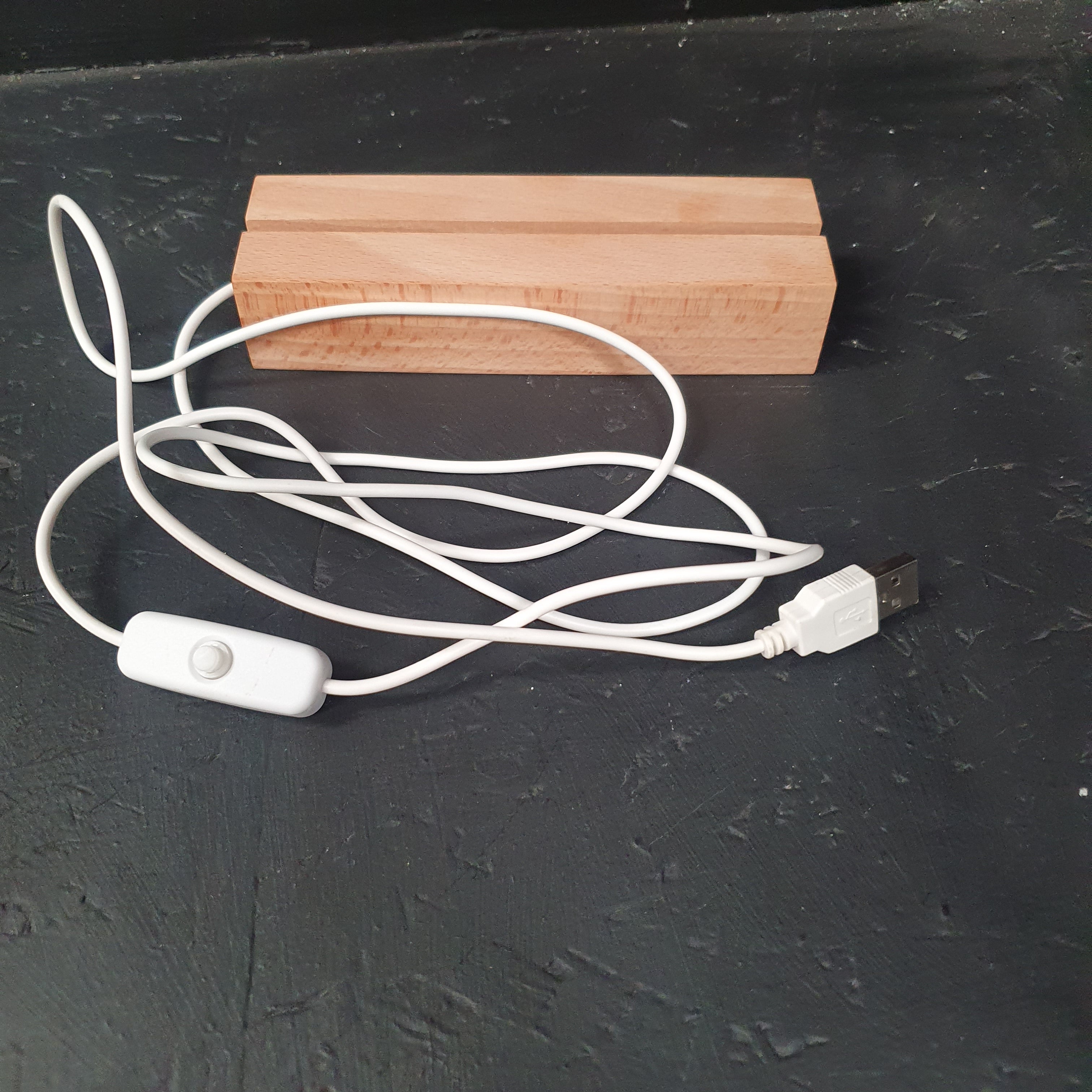 A white USB charging cable with an inline switch and wooden end caps, shown on a dark textured surface next to two small wooden blocks.