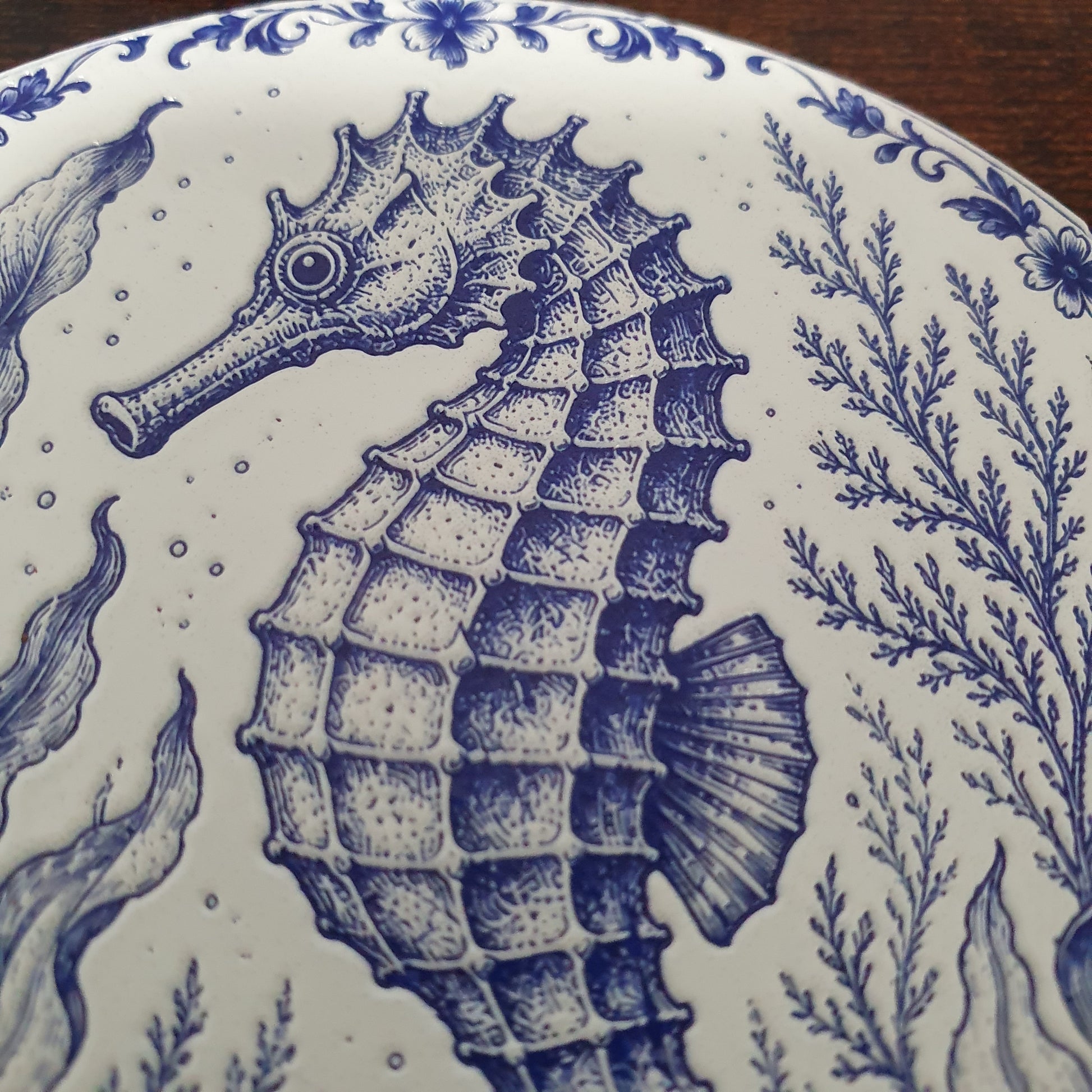 Close-up of a white ceramic coasters featuring a detailed blue seahorse and marine plant illustration in a classic Delftware style.