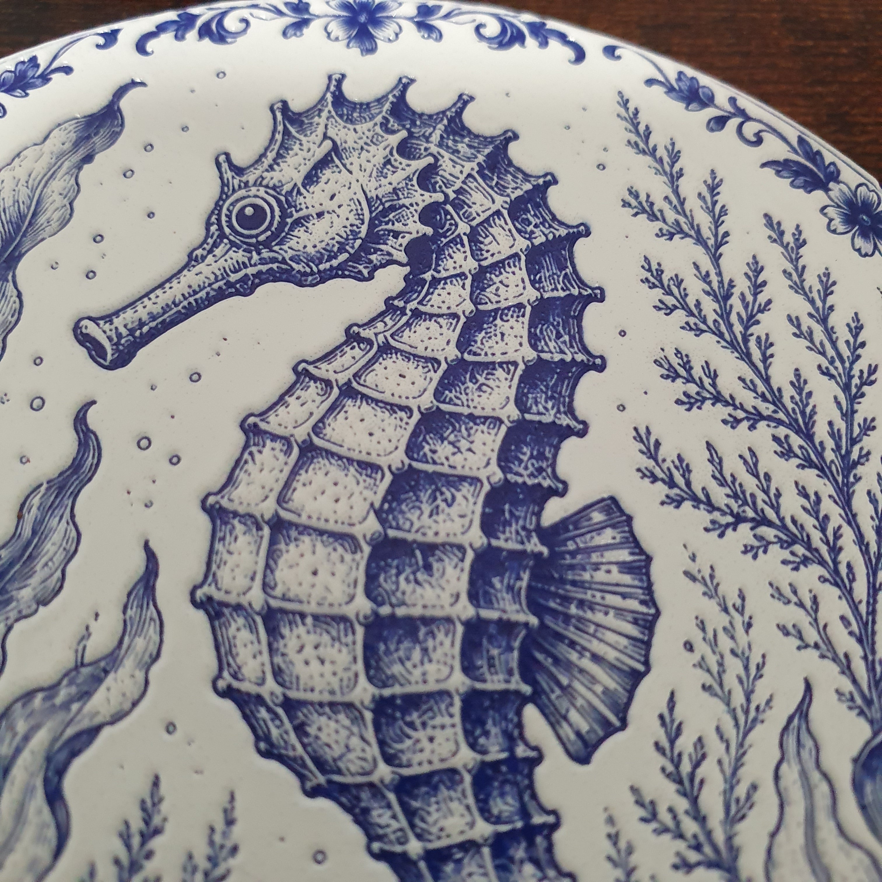 Close-up of a white ceramic coasters featuring a detailed blue seahorse and marine plant illustration in a classic Delftware style.