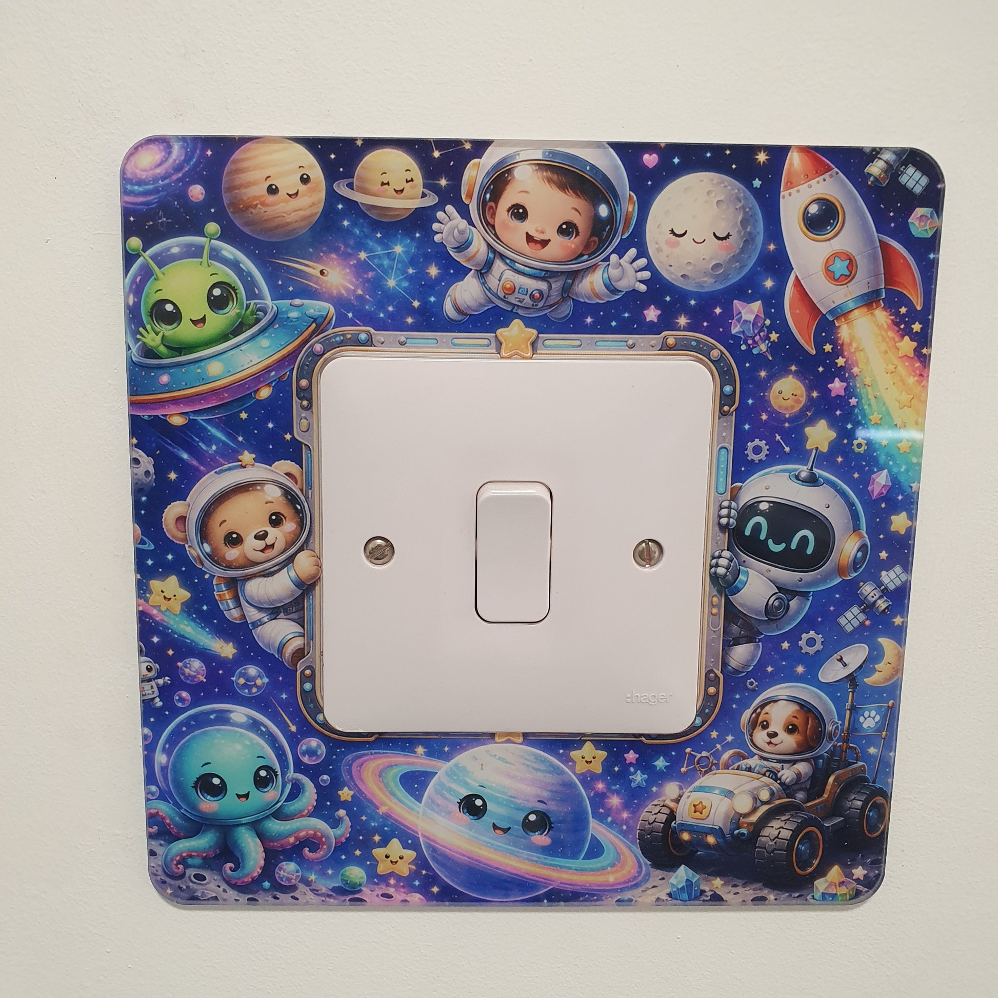 A square light switch plate cover featuring a colorful cartoon space theme with astronauts, planets, stars, and a rocket, shown installed over a white single-toggle switch on a plain light background.