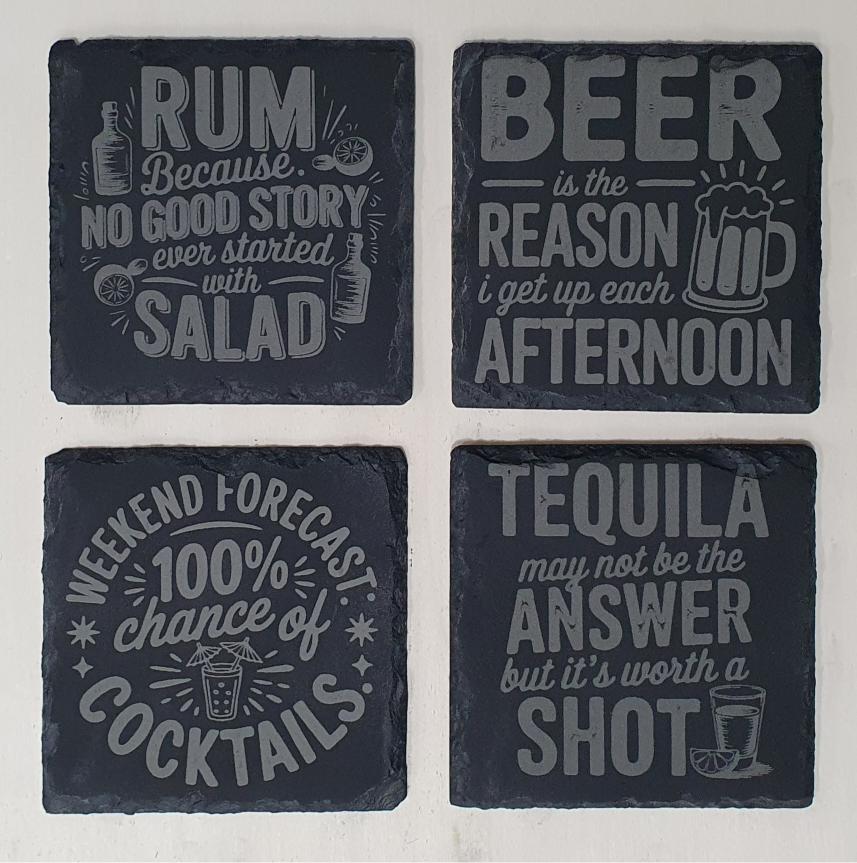 Four black slate coasters with humorous drink text designs on a white background