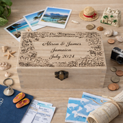 Personalised wooden honeymoon keepsake box engraved with names, destination and date, surrounded by travel photos and holiday souvenirs on a wooden desk.