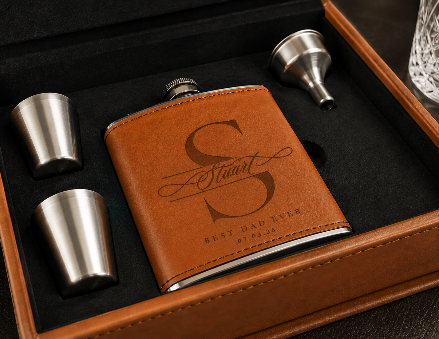 Personalized stainless steel flask gift set in a brown leather presentation box, featuring a brown leather flask cover engraved with a large monogram and 'Best Dad Ever' text, plus two metal shot glasses and a funnel.