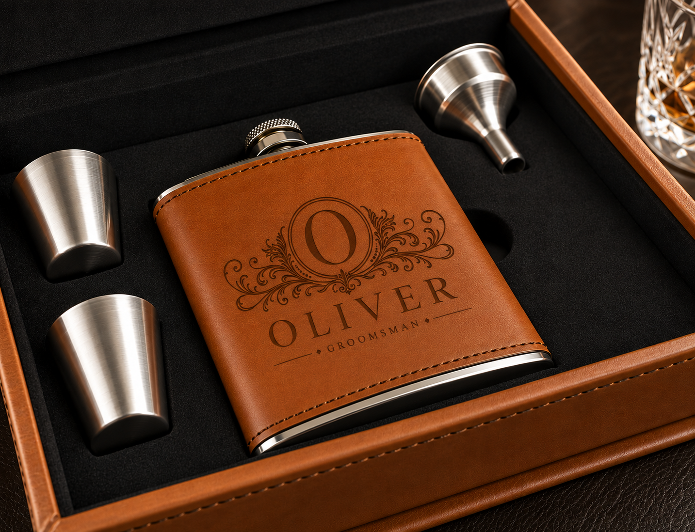 A personalized brass flask with a brown leather cover, shown inside a wooden presentation box with two metal shot glasses and a funnel. The flask is engraved with the name 'OLIVER' and 'GROOMSMAN'.