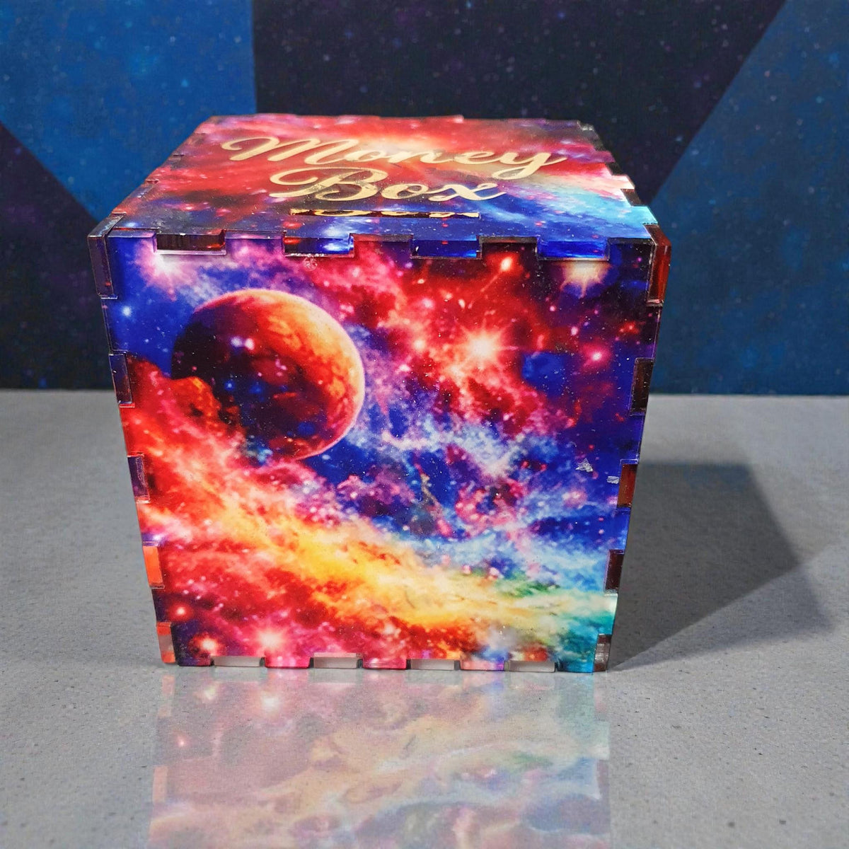 Side view of colourful space design money box showing detailed galaxy print with planets and nebula artwork. Acrylic savings box with interlocking corner joints, ideal as a gift or decorative piggy bank.
