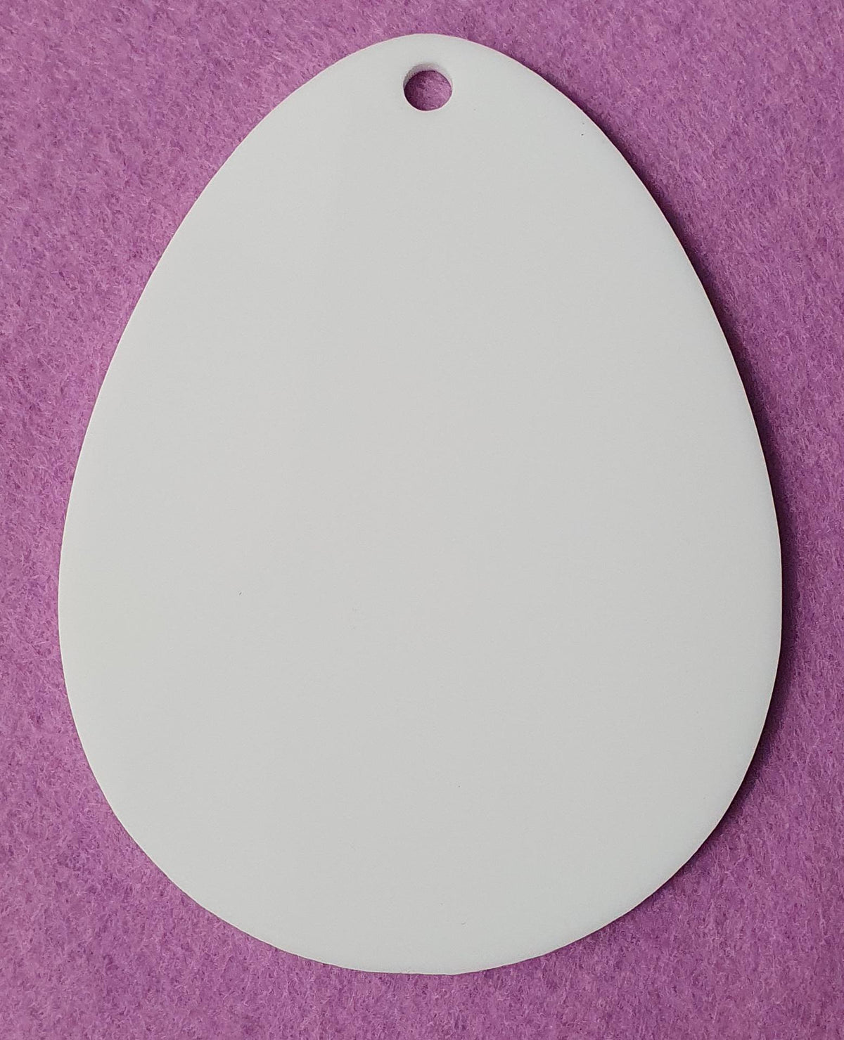 White cast acrylic Easter egg blank close up showing smooth surface, clean laser cut edges and top hanging hole suitable for vinyl, sublimation and UV printing.