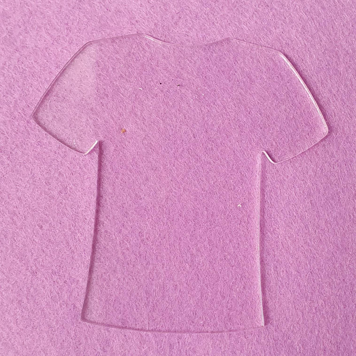 Clear acrylic shirt blank displayed on pink background highlighting transparent finish and clean cut outline suitable for vinyl and engraving.