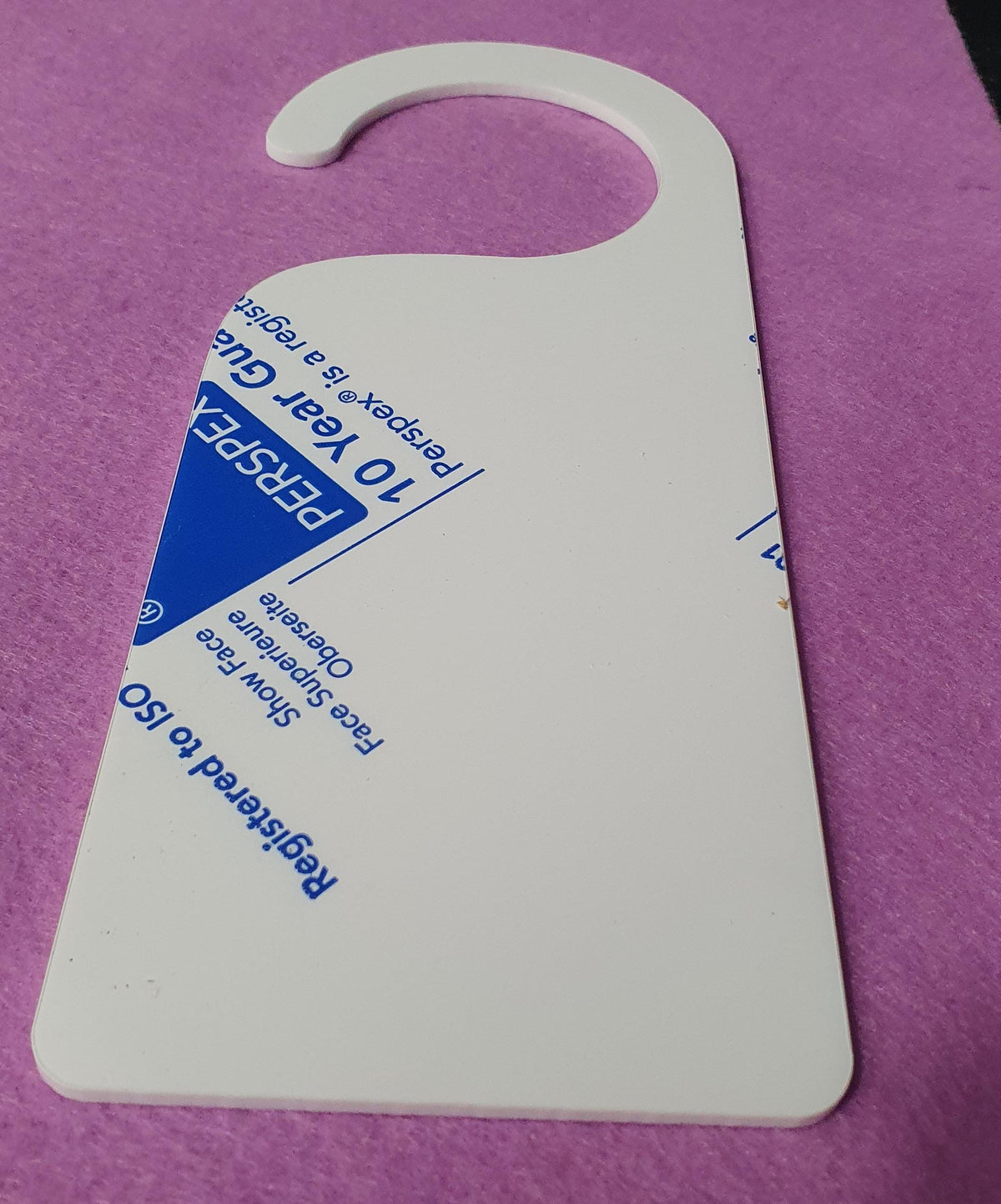 Close up angled view of white acrylic door hanger blank highlighting 3mm thickness, smooth surface finish and curved hook cut-out for standard door handles.
