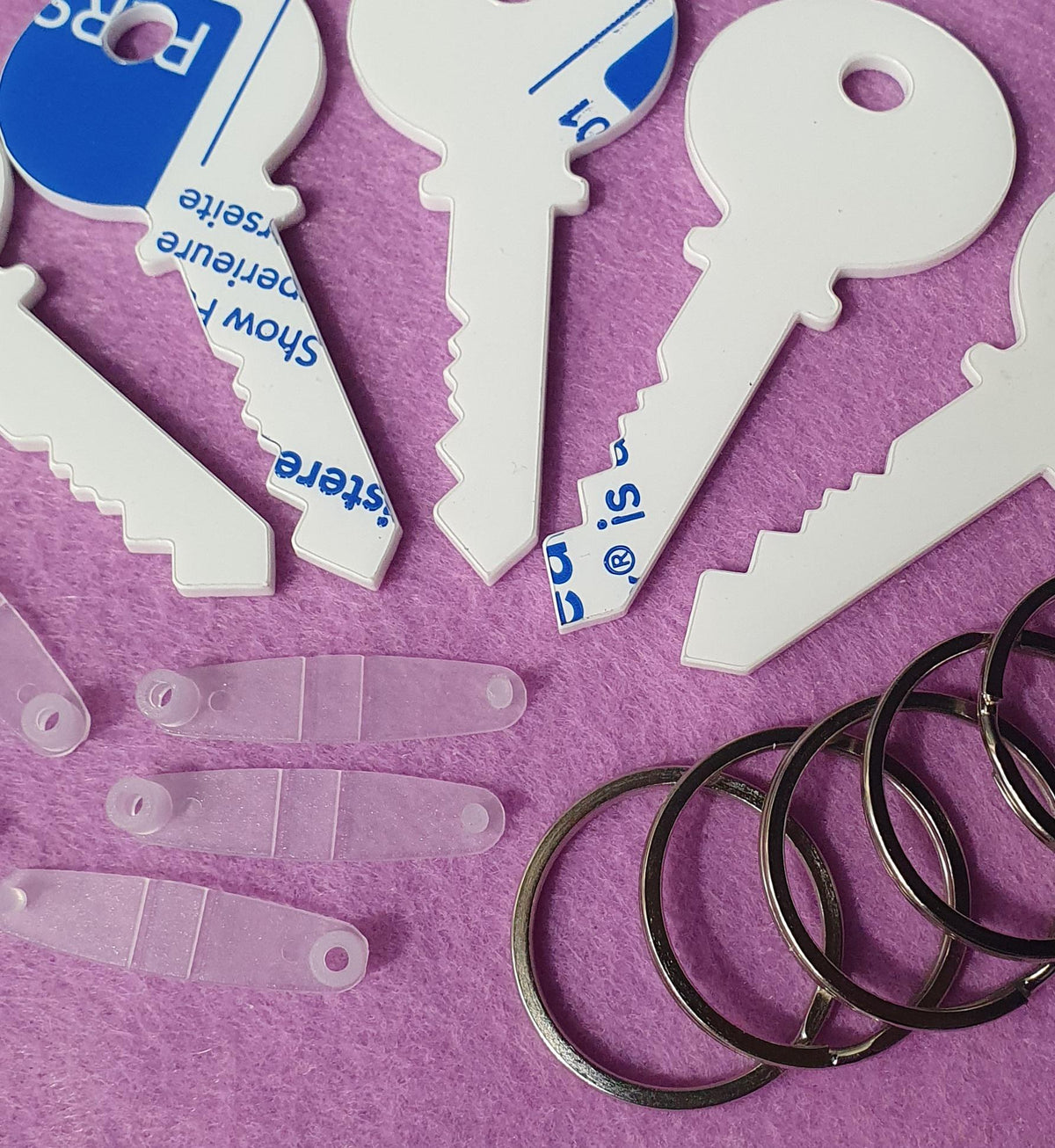 Close up of white acrylic key shape blank showing smooth surface, precision laser cut edges and protective film partially applied.