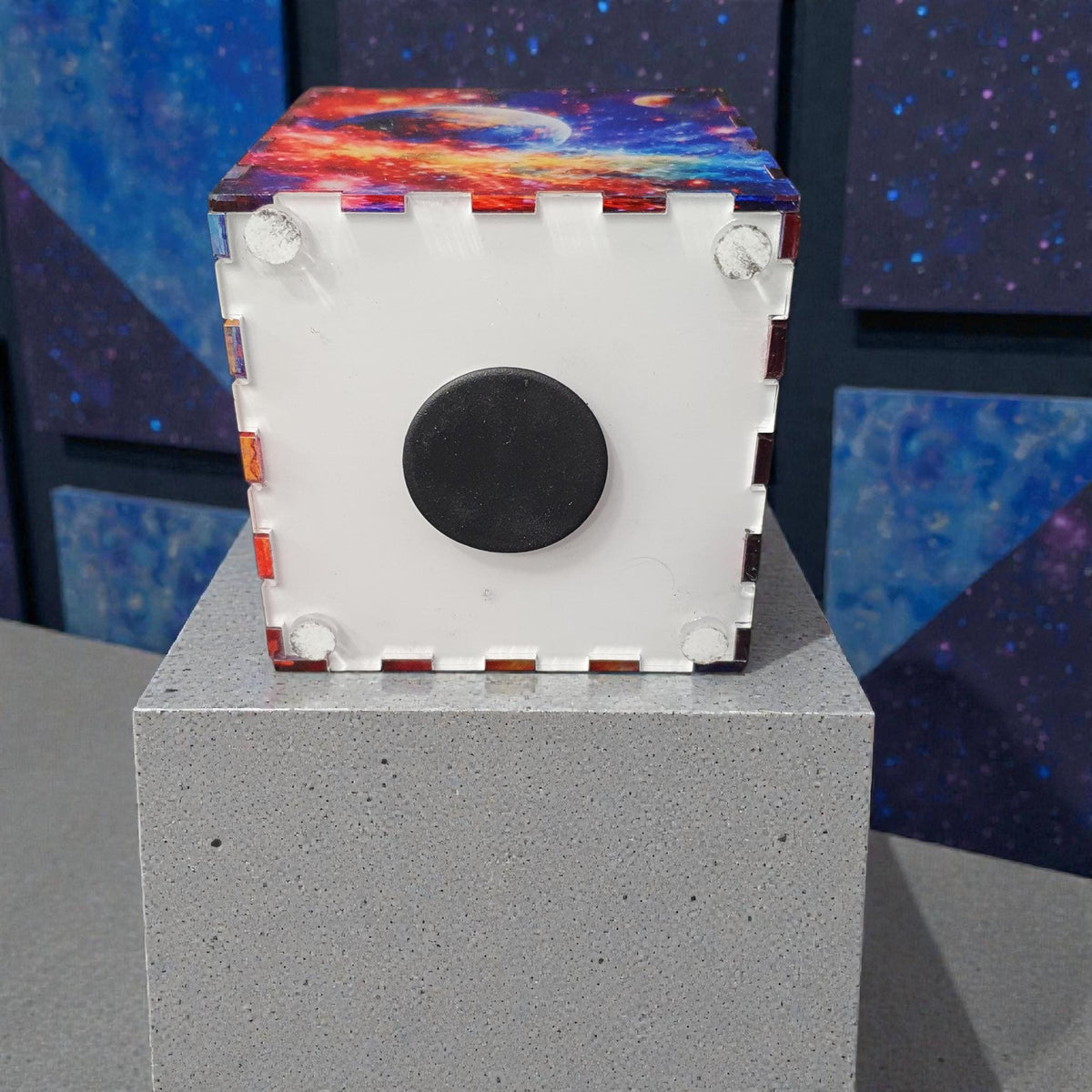 Bottom view of acrylic money box showing removable base with black rubber stopper for easy access to savings. Durable construction with interlocking panels and galaxy printed sides.