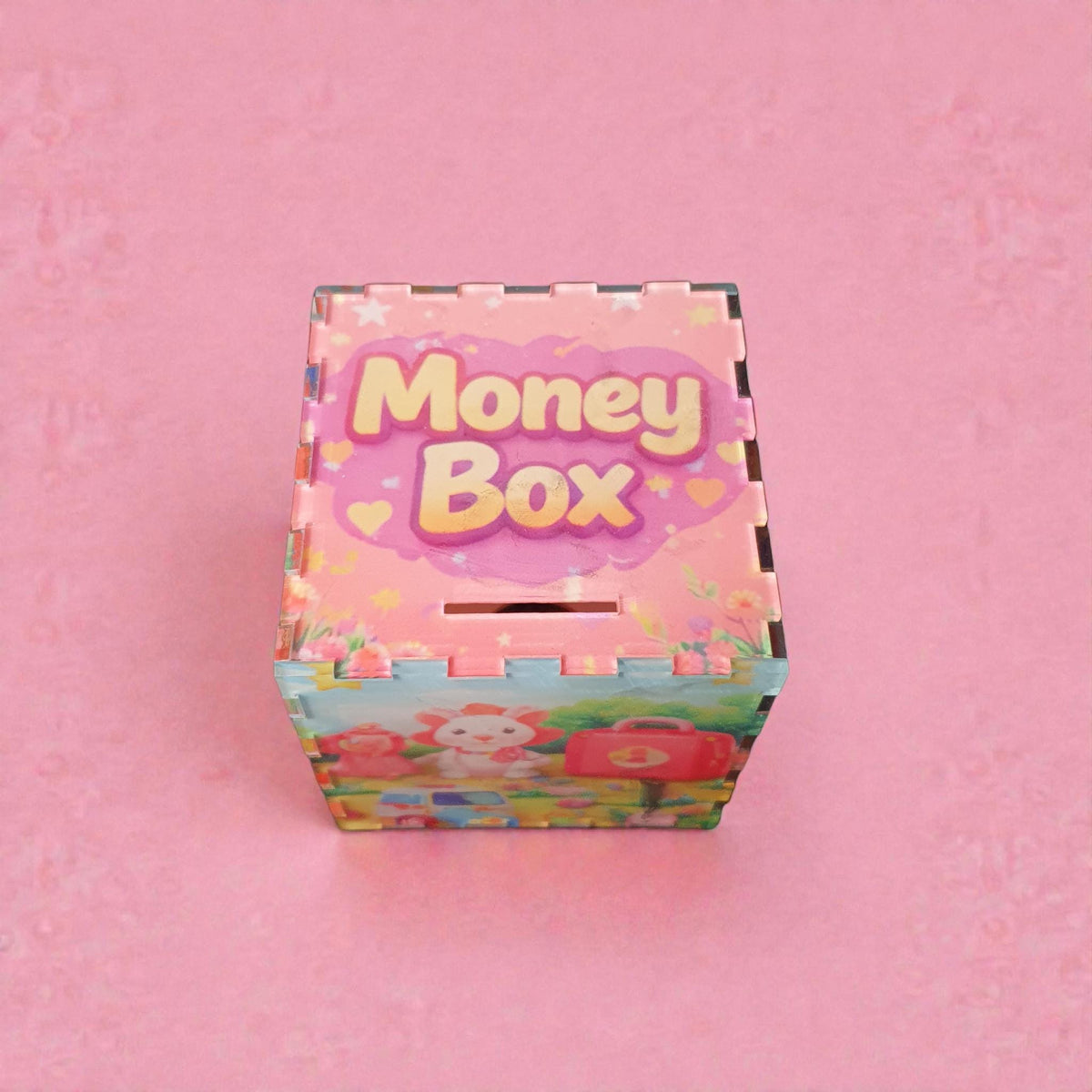 Pink children’s acrylic money box with “Money Box” printed on the lid, featuring pastel hearts and floral details. The sides show a cute bunny character and toy scene illustration. Decorative kids savings box displayed against a soft pink background.