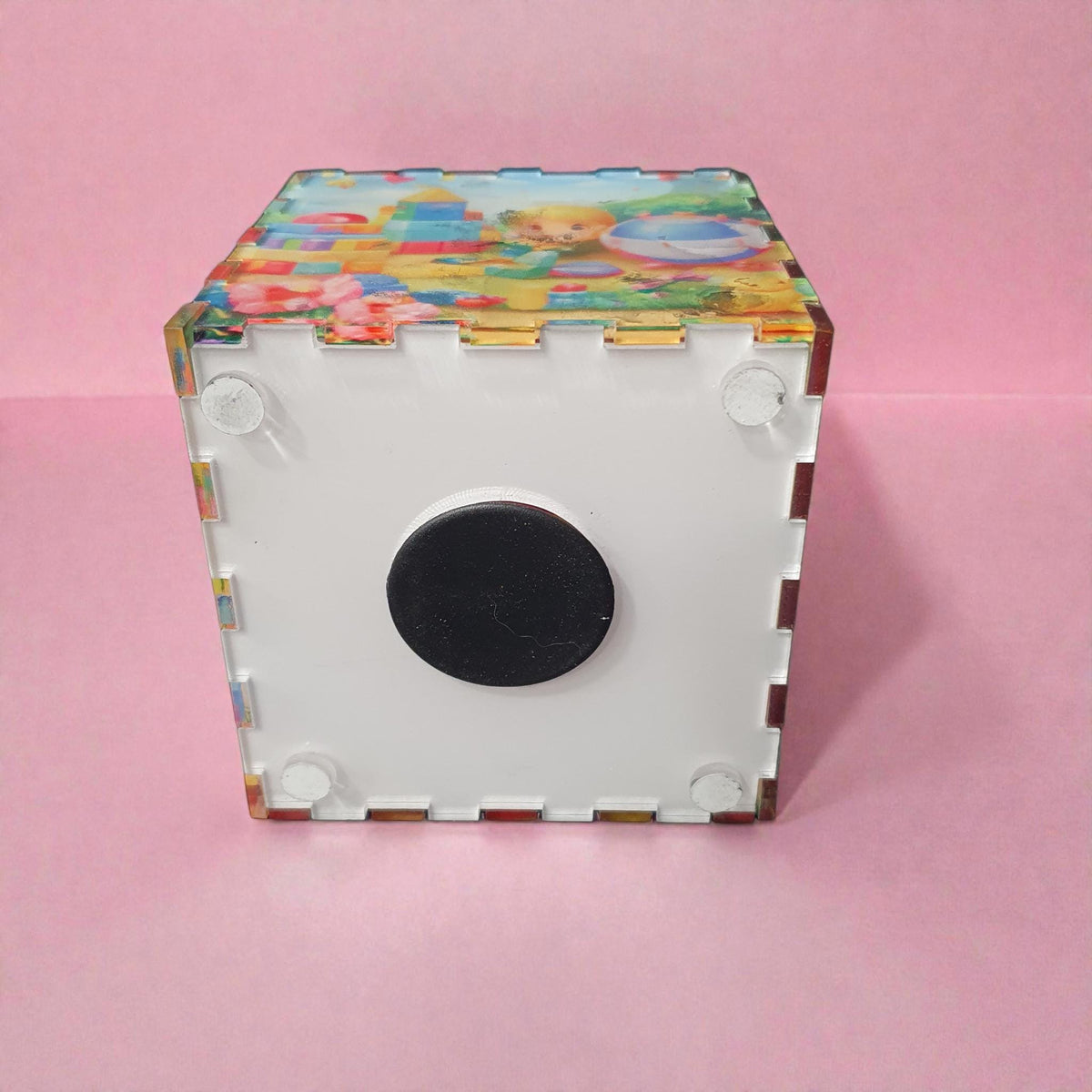 Bottom view of pink themed money box showing removable white base with black rubber stopper for easy access to coins. Durable acrylic construction with interlocking panels.