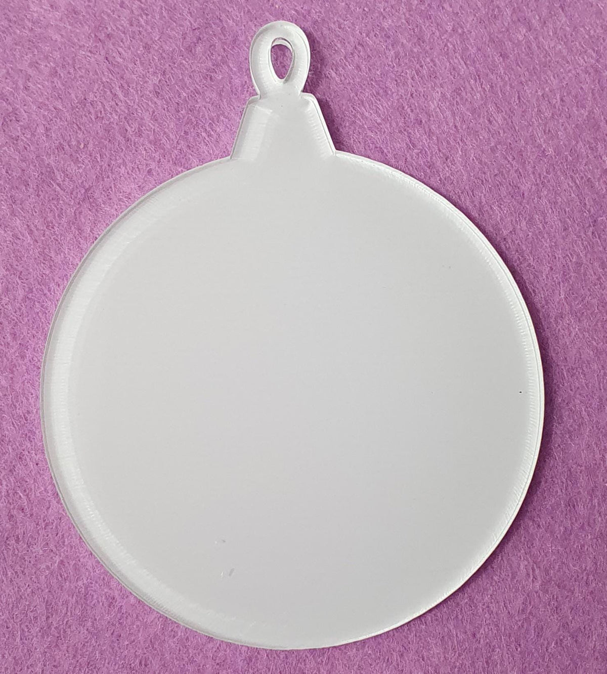 Clear acrylic bauble blank displayed on pink background highlighting transparent finish and integrated hanging loop for Christmas ornament crafting.