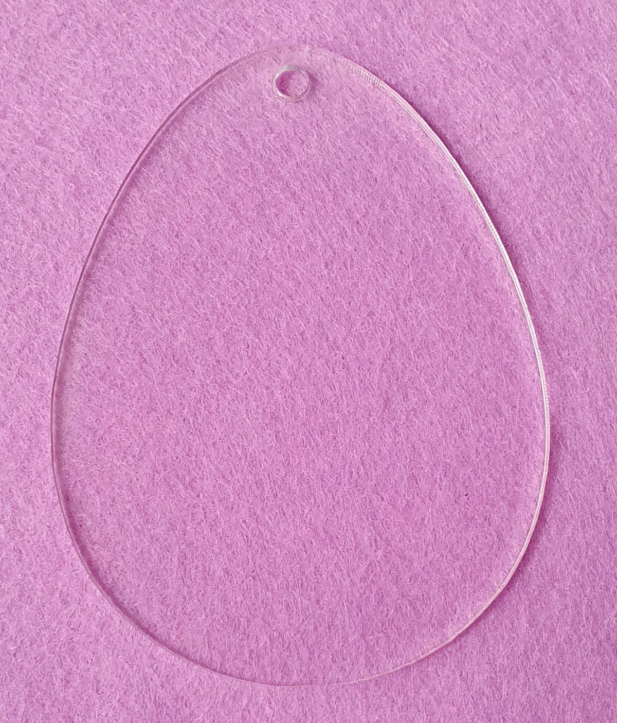 Clear acrylic Easter egg blank displayed on pink background highlighting transparent finish and precision cut shape ideal for personalised decorations.