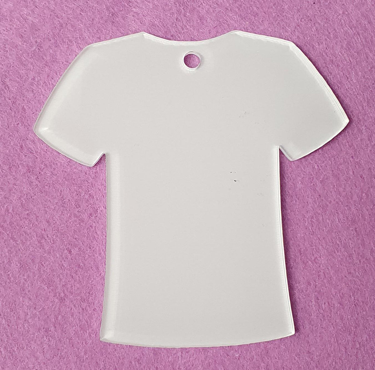 White cast acrylic T-shirt shape blank close up showing smooth surface, precision laser cut edges and top hole for hanging decoration.
