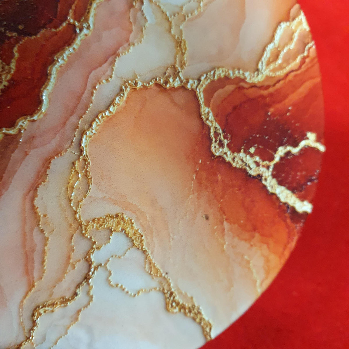 Terracotta marble effect coaster with textured gold veining held in hand, round 10cm cork backed drink coaster warm home decor