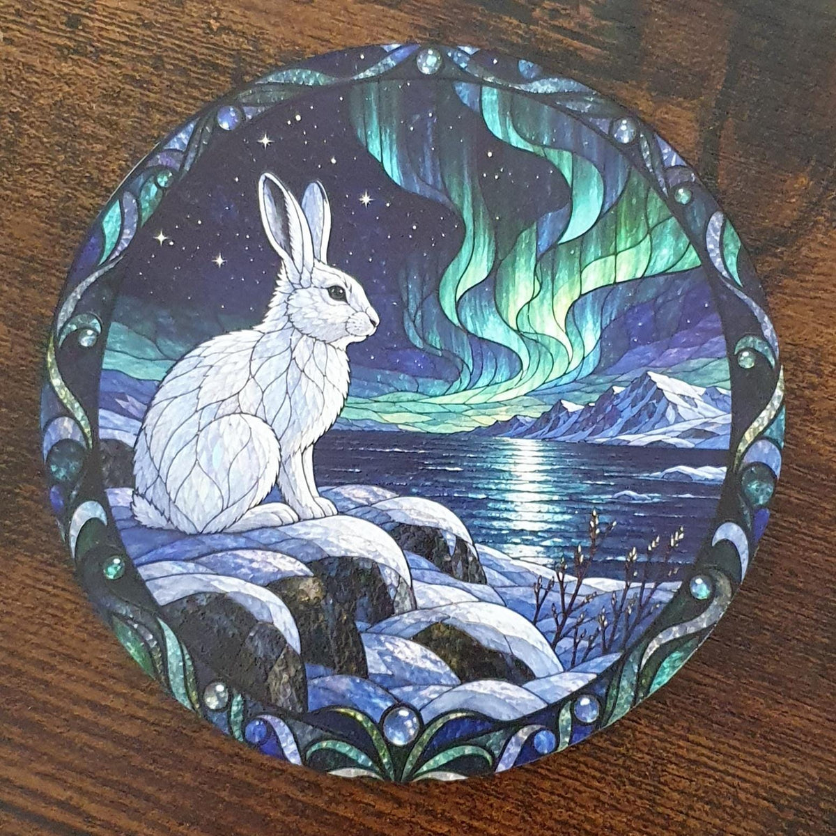 Beautiful Arctic hare stained-glass effect coaster sitting on snowy rocks overlooking frozen waters beneath glowing Northern Lights.
