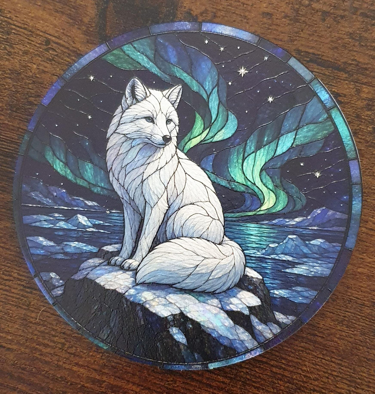 Arctic fox stained-glass effect coaster sitting on snowy rocks beneath vibrant green Aurora Borealis with frozen ocean and mountain scenery.