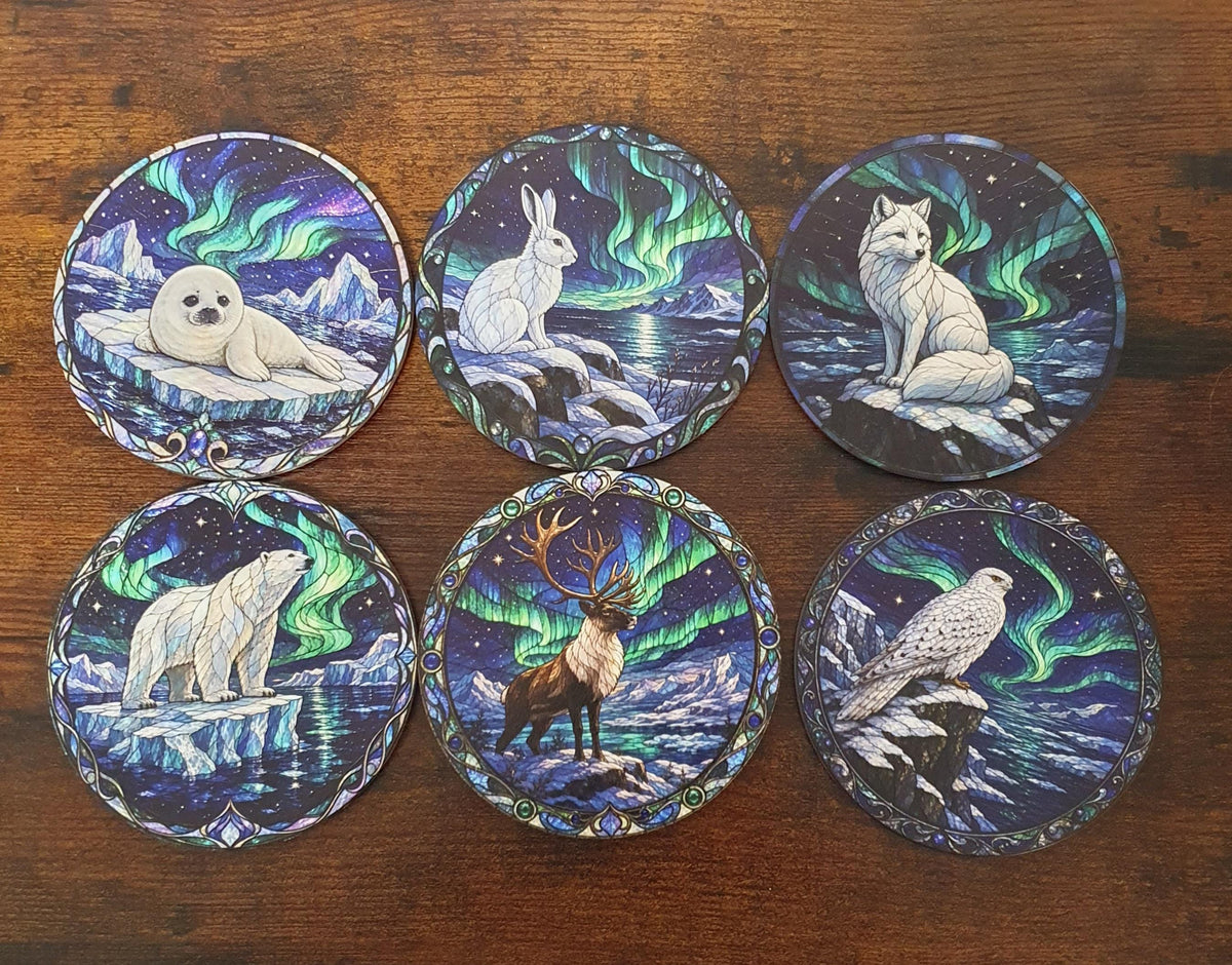 Complete collection of six stained-glass Arctic animal coasters featuring baby seal, polar bear, Arctic fox, hare, snowy falcon and reindeer beneath colourful Northern Lights.
