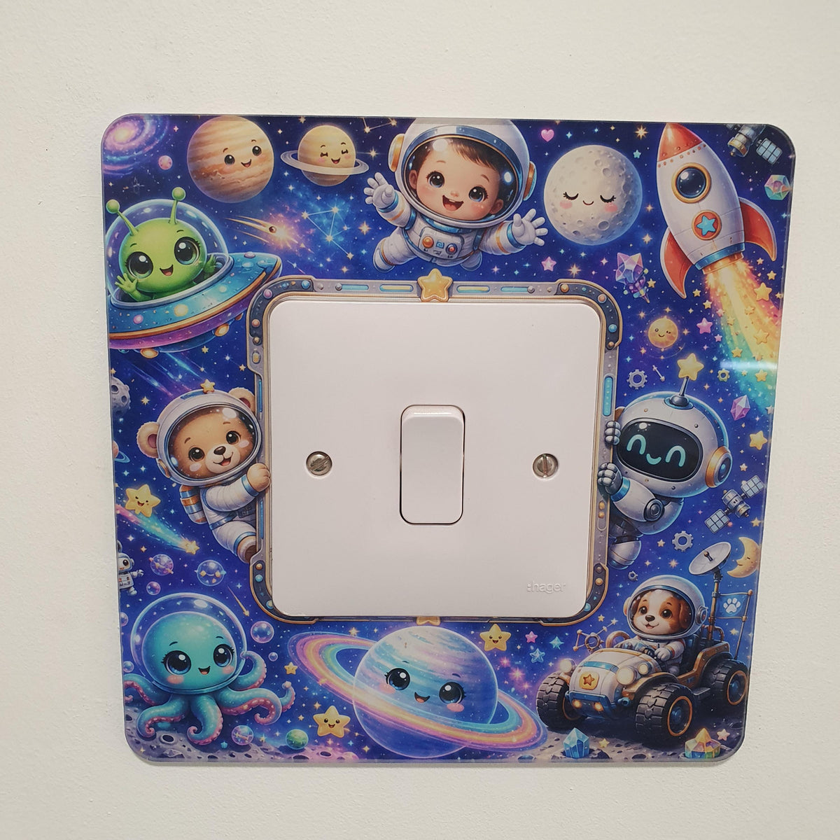 Colourful space-themed children's light switch surround featuring cute astronauts, rockets, smiling planets, aliens and stars surrounding a standard UK light switch.