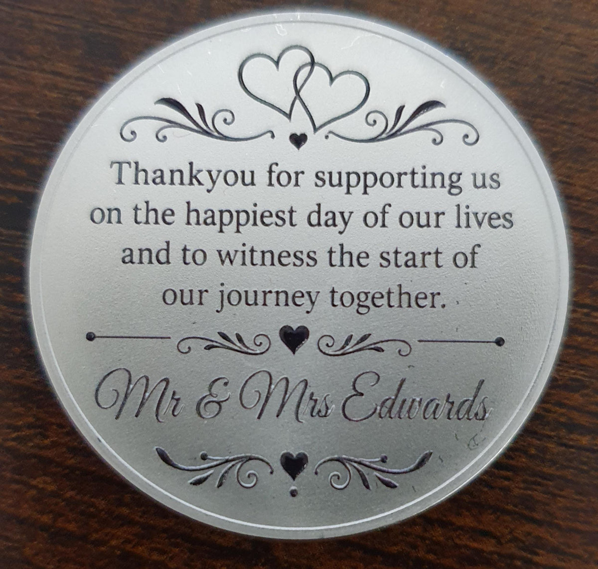 Elegant engraved wedding favour coin with decorative hearts and floral scroll detailing.