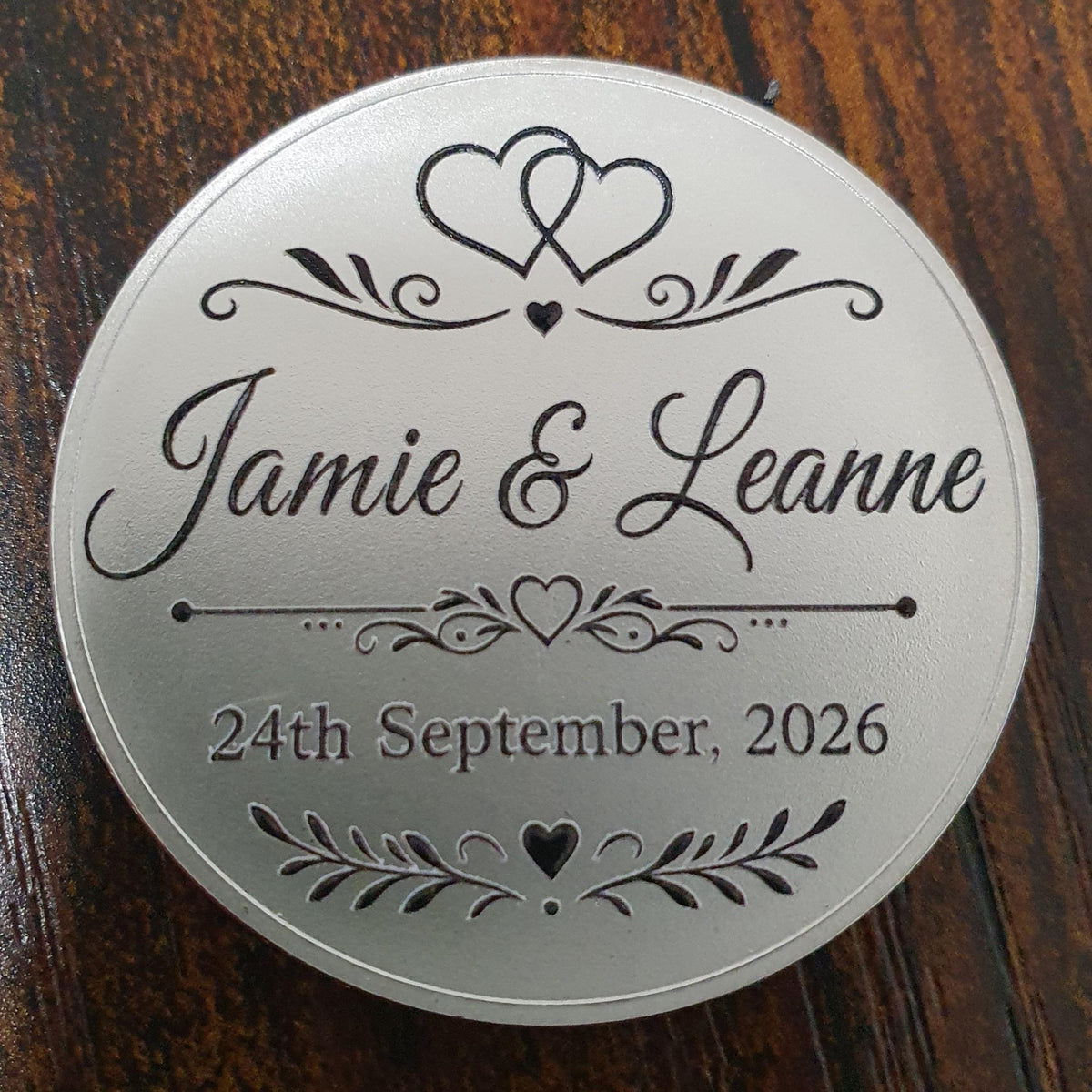 Elegant engraved wedding favour coin with decorative hearts and floral scroll detailing.