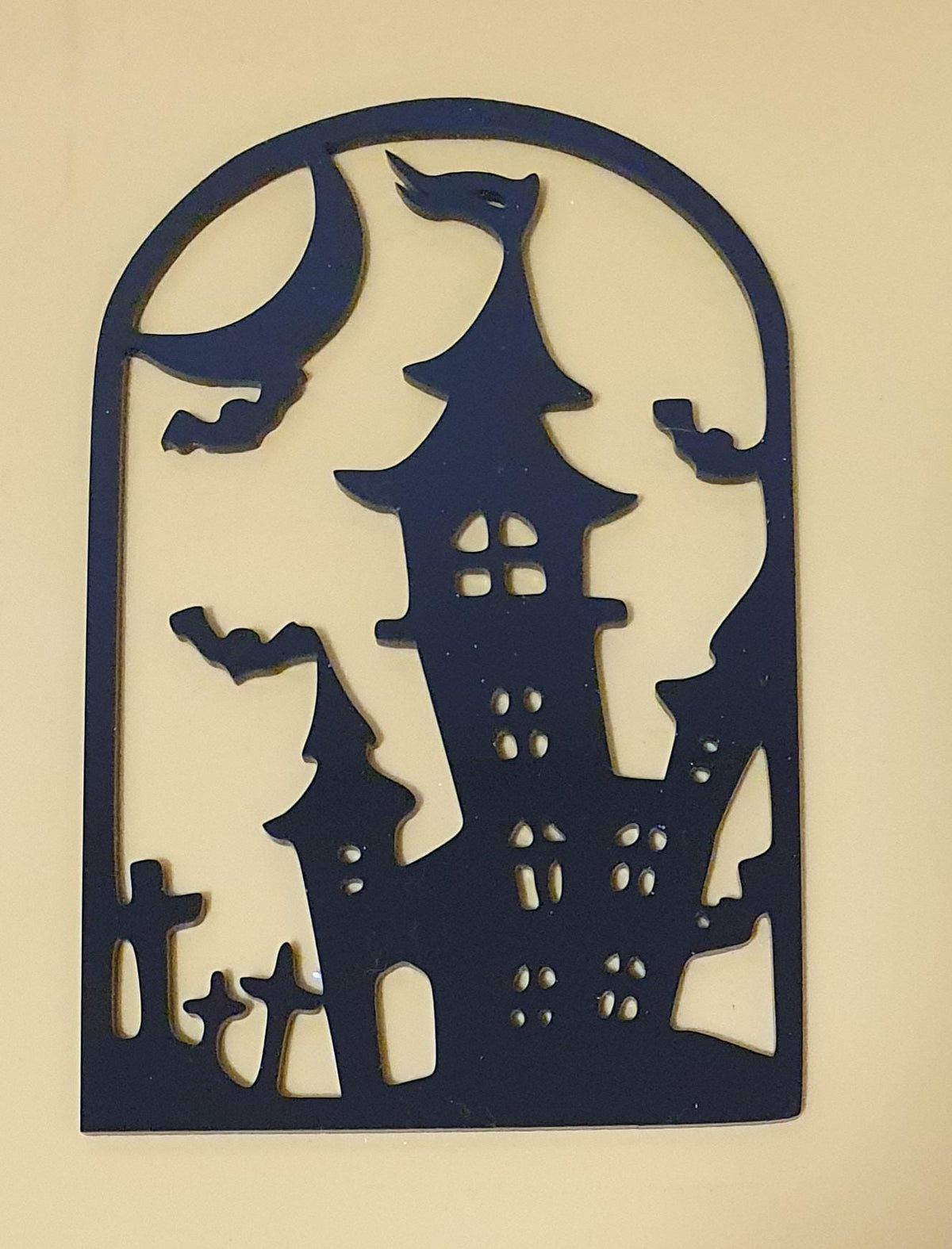 Black laser-cut acrylic Halloween decoration featuring a haunted gothic castle, flying bats and gravestones in an arched frame.