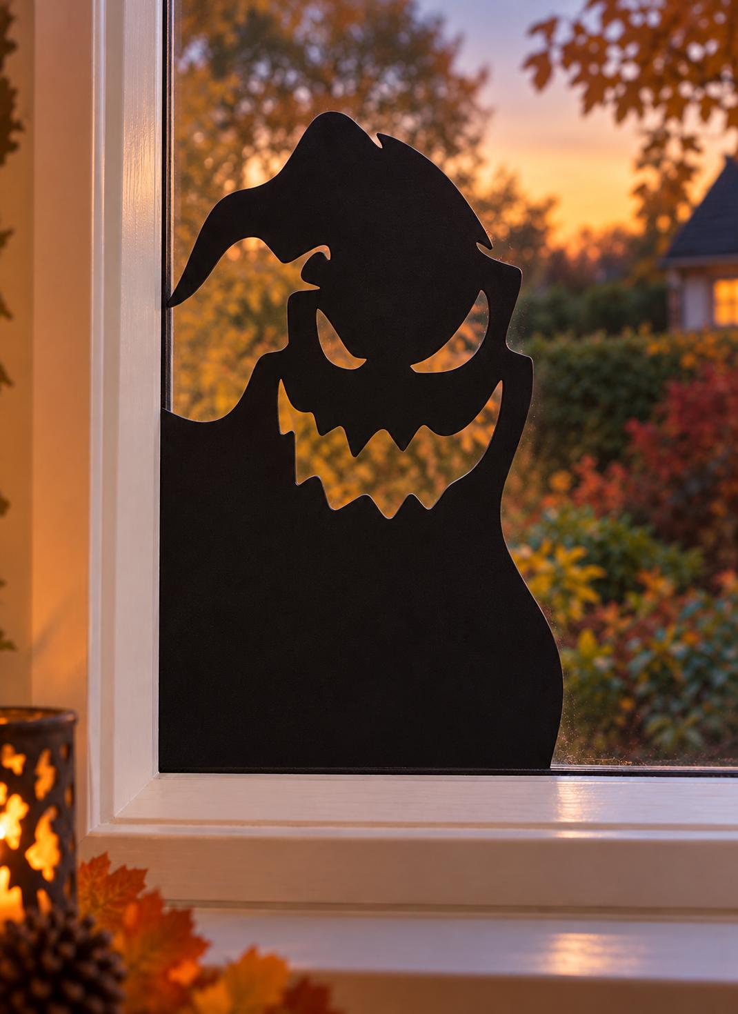 Black Halloween ghost window decoration displayed in the lower corner of a white-framed window, featuring pointed eyes and a jagged spooky grin.