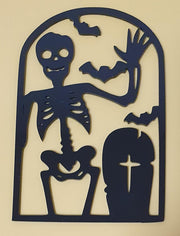 Black laser-cut acrylic Halloween decoration featuring a waving skeleton, flying bats, a spooky pumpkin and a cross gravestone in an arched frame.
