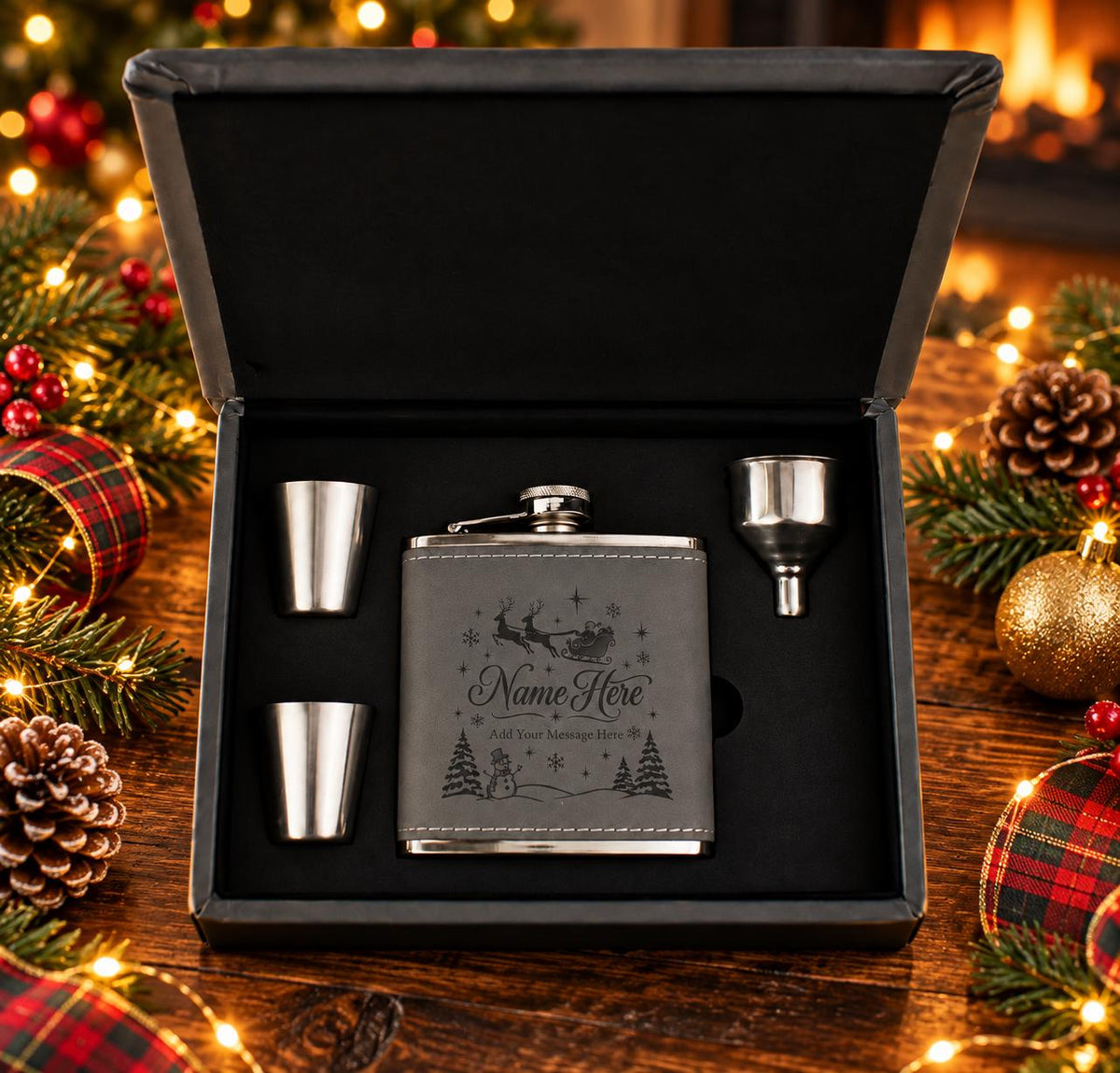 Open grey Christmas flask gift box on a festive table, showing the engraved Santa design, two stainless steel cups and a funnel.
