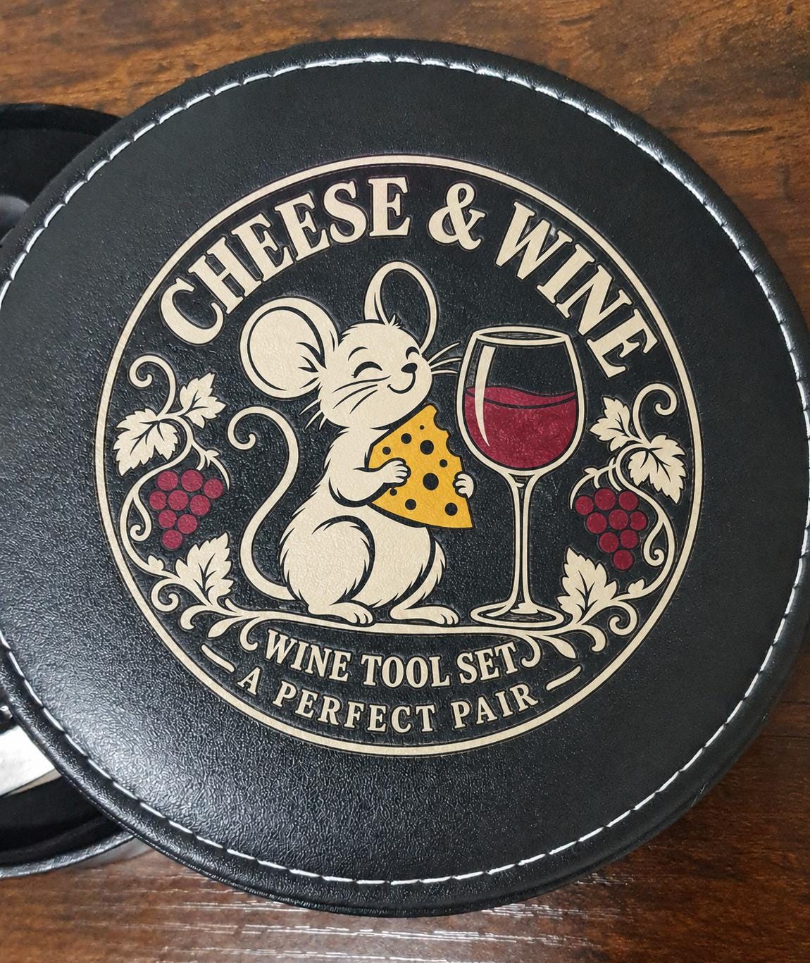 Close-up of the black case lid with a mouse holding cheese beside a glass of red wine and “A Perfect Pair” text.
