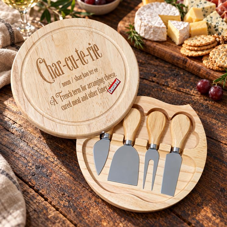 Round wooden cheese board with funny engraved charcuterie definition and four cheese tools stored neatly in the open base.