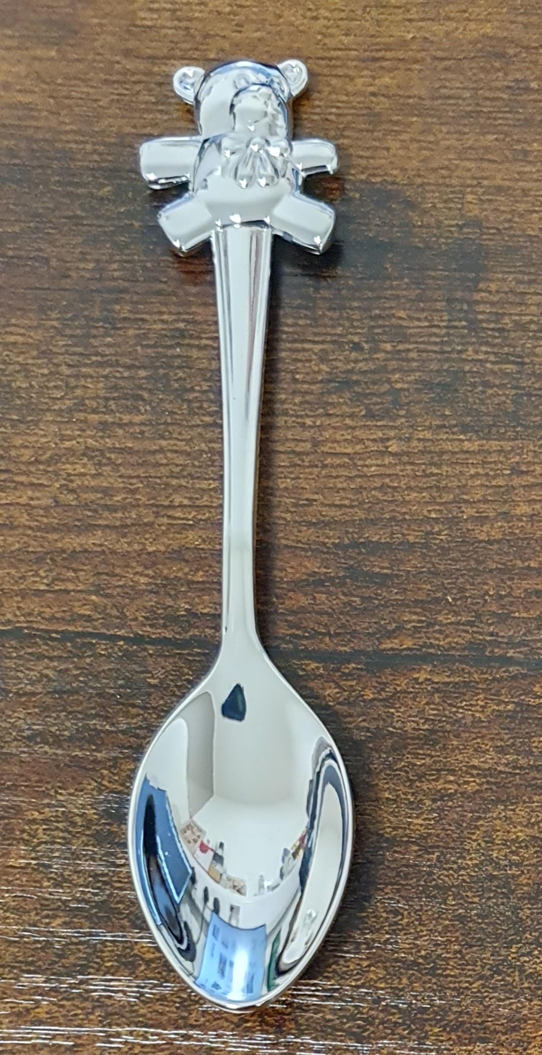Close-up of the silver plated teddy bear handle decoration, showing its rounded ears, outstretched arms and small bow.