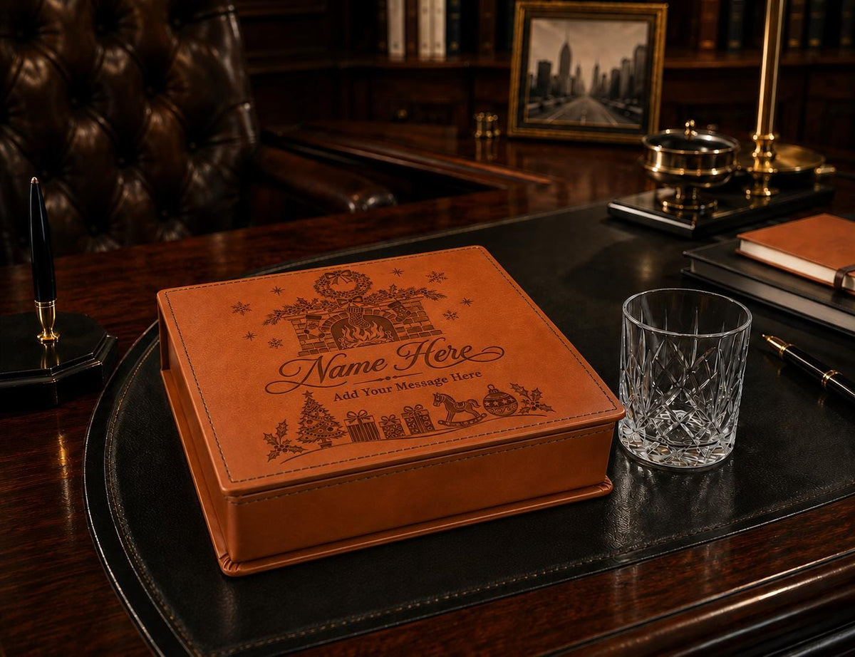 Brown personalised Christmas gift box with a fireplace engraving on the lid, displayed beside a drinking glass on a desk.