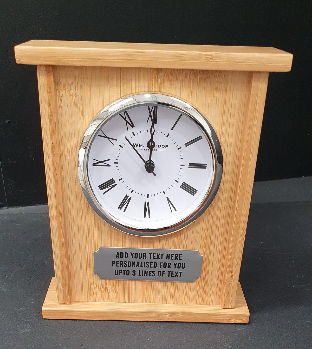 Front view of a bamboo mantel clock with a silver-toned Roman numeral face and personalisation plaque.