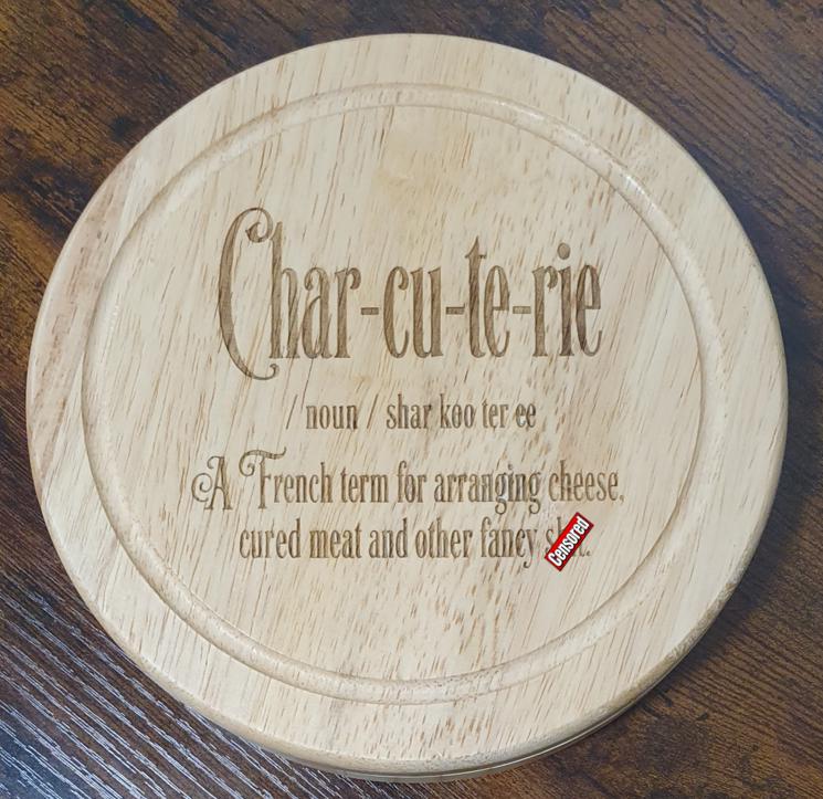 Funny cheese board and tool set on a rustic wooden table beside a separate serving board with cheeses and crackers.
