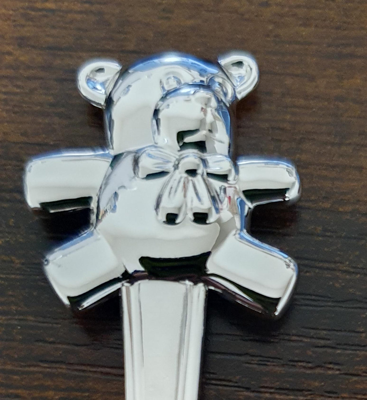 Close-up of the silver plated teddy bear handle decoration, showing its rounded ears, outstretched arms and small bow.