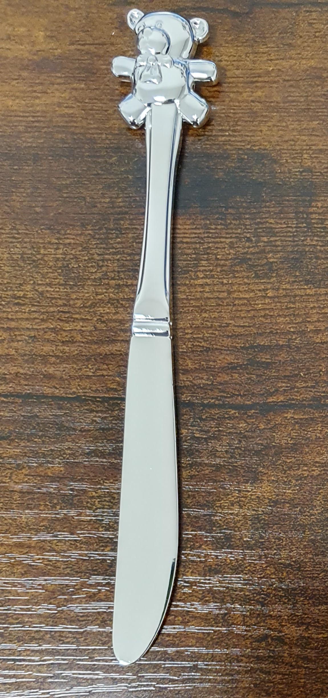 Silver plated with a rounded blade and teddy bear topped handle, shown on a brown wooden surface.
