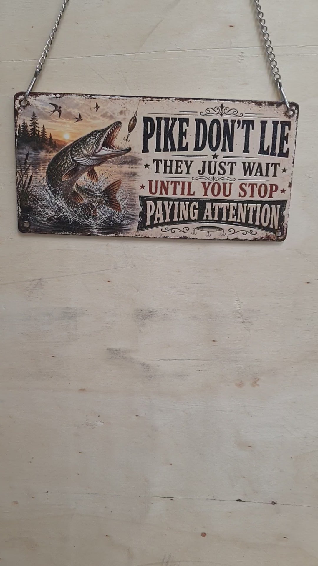 Load video: Funny "Pike Don't Lie" acrylic hanging fishing sign featuring a leaping Northern Pike and vintage distressed artwork, complete with metal hanging chain for man caves, fishing lodges and anglers.