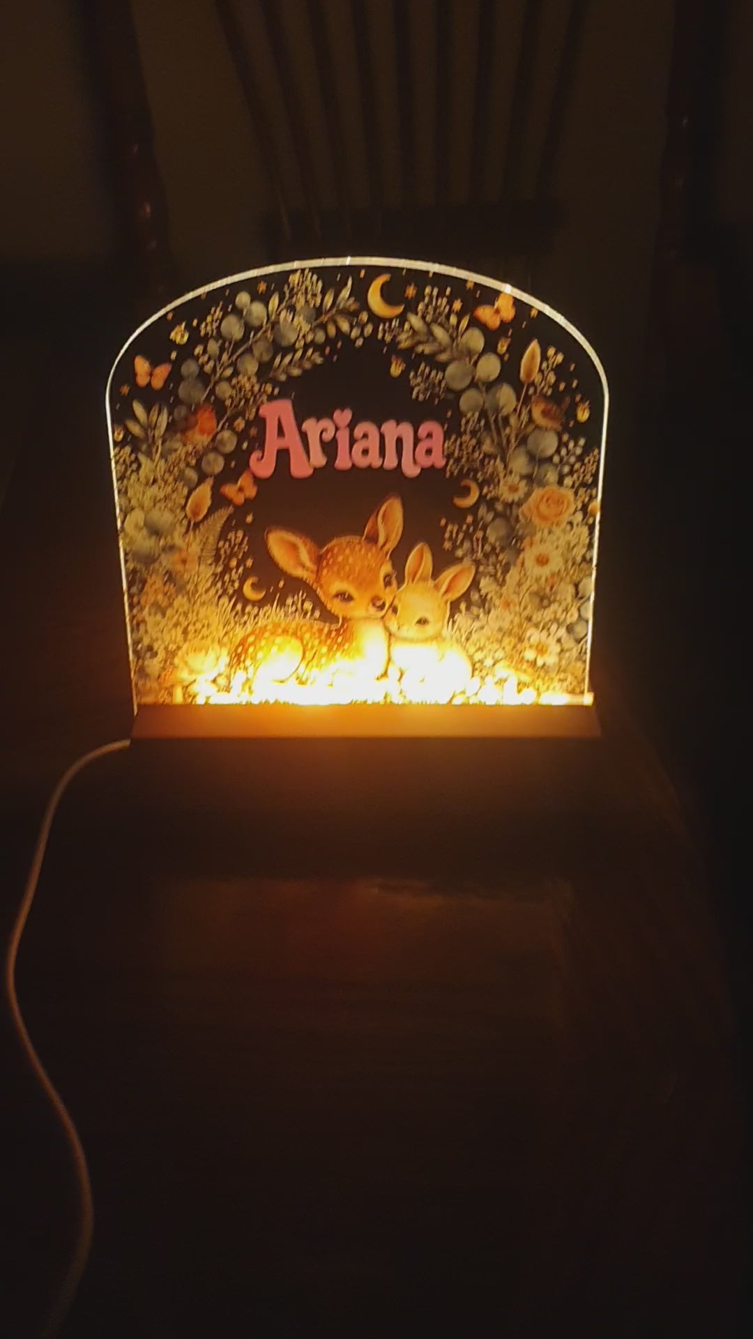 Load video: Custom acrylic nursery night light with personalised name and adorable deer and bunny artwork, surrounded by flowers, butterflies, birds and woodland foliage.