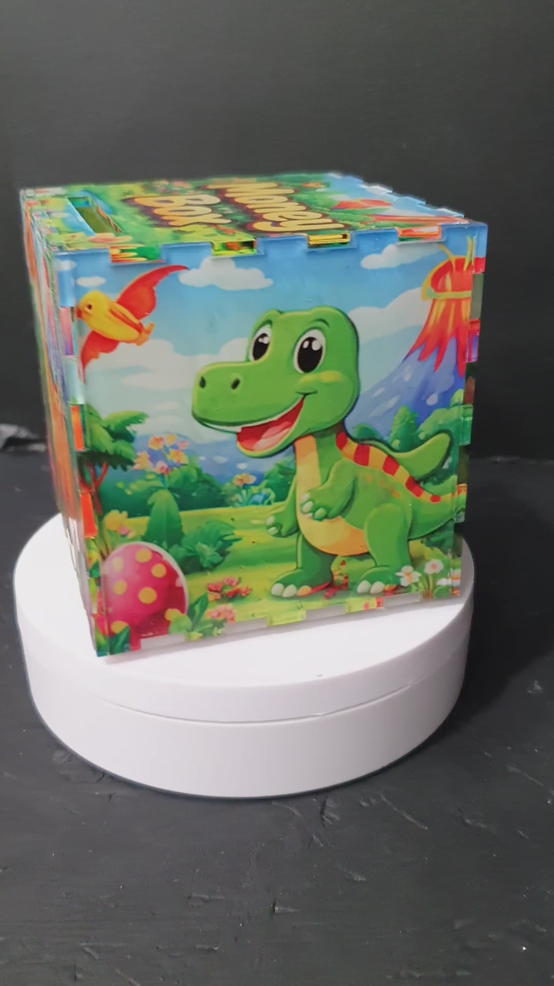 Load video: Front view of baby dino money box with “Money Box” text on lid and coin slot, colourful nursery savings bank.